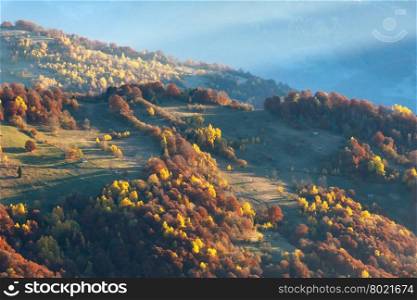 Sunbeam and autumn misty morning mountain view with colorful trees on slope.