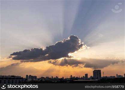 Sunbeam through the dramatic cloud during sunset time, with silhouette building below