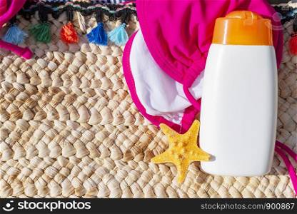 Sunblock lotion bottle with bikini and starfish on floor. Summer travel concept background.