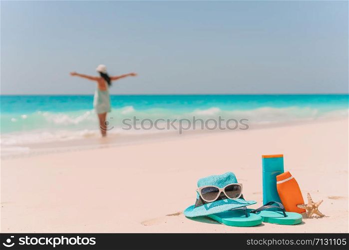 Suncream bottles, goggles, starfish on white sand background ocean and young woman. Suncream bottles, sunglasses, flip flop on white sand background ocean