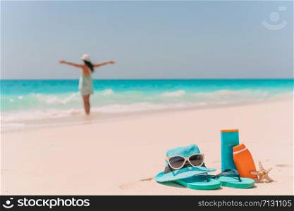 Suncream bottles, goggles, starfish on white sand background ocean and young woman. Suncream bottles, sunglasses, flip flop on white sand background ocean
