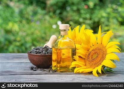 Sunflower seeds and flowers with a bottle of oil on a wooden table. Natural green background. Natural green background. Sunflower seeds and flowers with bottle of oil on wooden table
