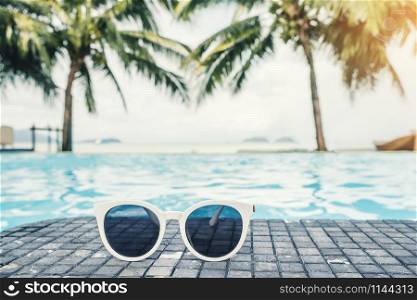 Sunglass on luxury swimming pool tropical beach resort , summer concept