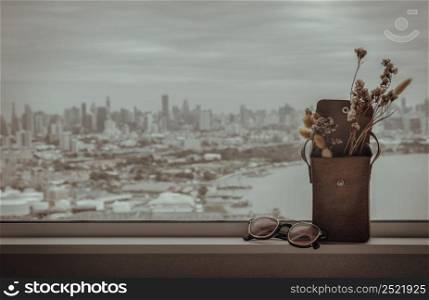 Sunglasses and Dried flowers in mini brown leather bag. Background it city and river view, Vintage tone style, Copy space for text, Selective focus.