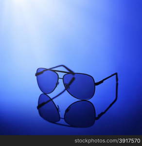 Sunglasses in blue light on a reflective background.