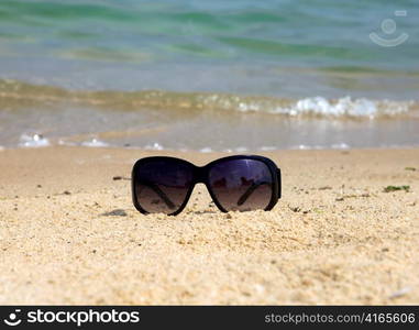 Sunglasses lay on sand at edge of sea