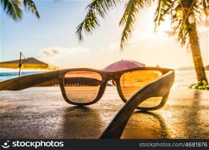 Sunglasses on beach. Sunglasses on tropical beach with palms at sunset