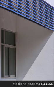 Sunlight and shadow on surface of blue steel trellis sunshade with glass window on white building wall in vertical frame 
