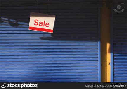 Sunlight and shadow on surface of hanging sale sign board in front of blue automatic shutter door of shop house