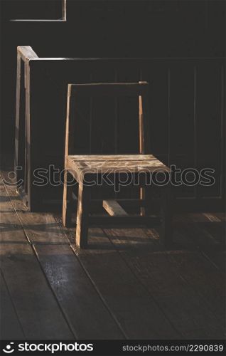 Sunlight and shadow on surface of the old empty wooden chair near the railing inside of vintage wooden house in dark tone style
