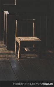 Sunlight and shadow on surface of the old empty wooden chair near the railing inside of vintage wooden house in dark tone style