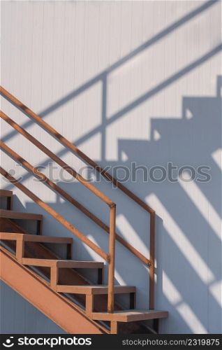 Sunlight and shadow on surface of the old outside metal staircase with gray sandwich panel wall of cold storage in freezer warehouse area