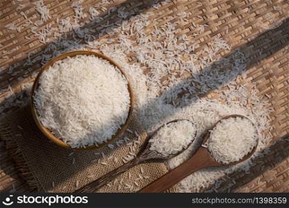 Sunlight and shadow on surface of white rice (Thai Jasmine rice) in ceramic bowl with wooden spoons on threshing basket, top view with copy space