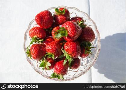 Sunlit bowl with fresh strawberries on a table with a white cloth