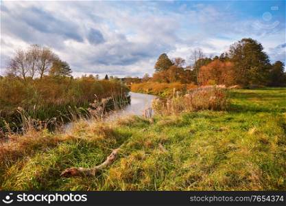 Sunny autumn day on river and meadow. Colorful landscape with forest, field, lake. Scenic fall rural landscape. Belarus