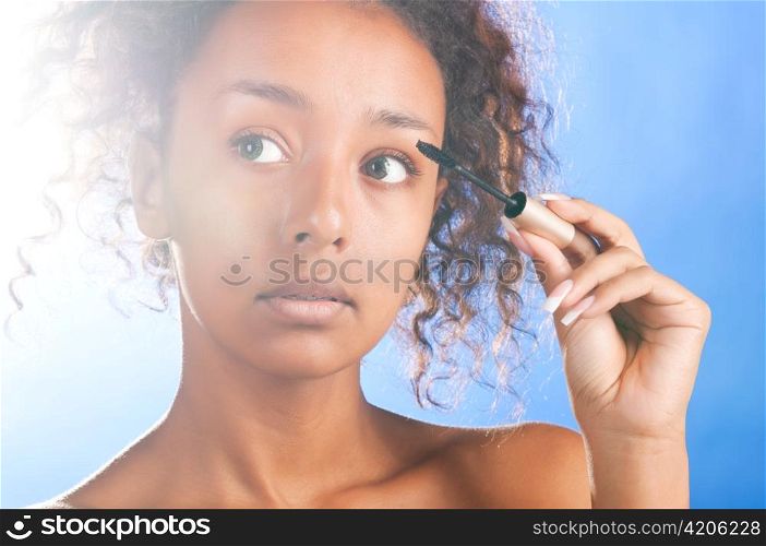 sunny beautiful mulatto woman is applying mascara, on sky background