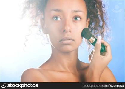 sunny beautiful mulatto woman is applying powder with brush, on sky background