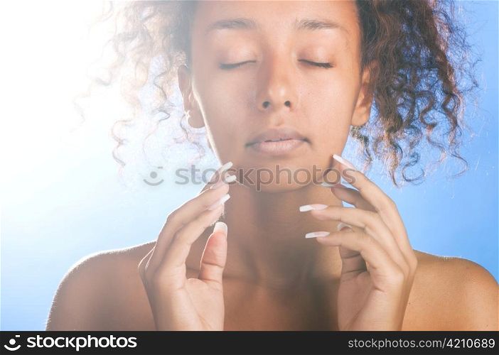 sunny beautiful mulatto woman with closed eyes on sky background