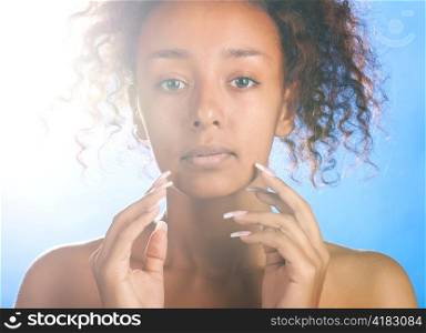 sunny beautiful mulatto woman with is touching her face and looking at camera on sky background