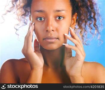 sunny beautiful mulatto woman with is touching her face and looking at camera on sky background