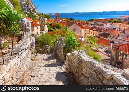Sunny beautiful view of red roofs, Old city street with stone stairs and church in town and port Omis, very popular tourist spot in Croatia. Sunny town and port Omis, Croatia