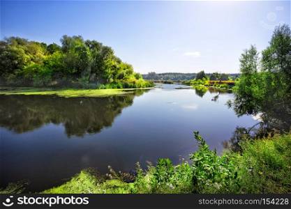Sunny day on the river with green trees on the shore. Summer landscape.. Sunny day on the river with green trees on the shore