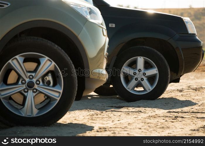 Sunny day. Sand and grass in the background. Two SUVs are. Front wheels are close up. Two SUVs Parked on the Sand