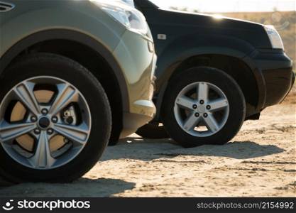 Sunny day. Sand and grass in the background. Two SUVs are. Front wheels are close up. Two SUVs Parked on the Sand
