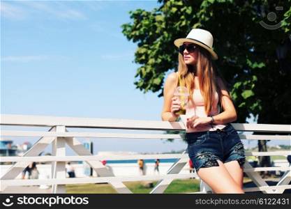 Sunny lifestyle fashion portrait of young stylish hipster woman walking on the street, wearing trendy outfit, hat, drinking tasty smoothie, travel with backpack.