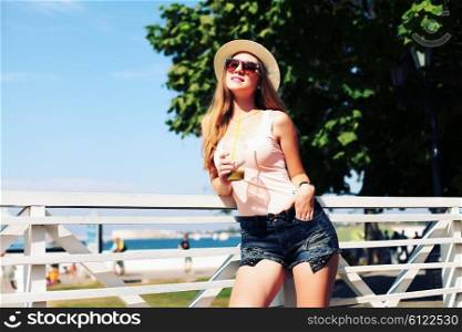 Sunny lifestyle fashion portrait of young stylish hipster woman walking on the street, wearing trendy outfit, hat, drinking tasty smoothie, travel with backpack.