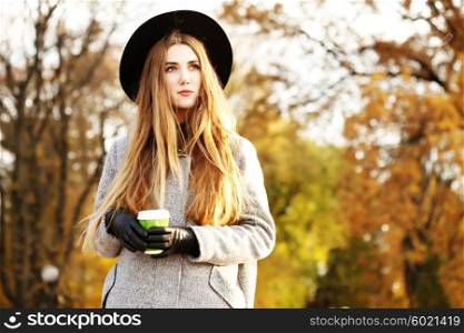 Sunny lifestyle portrait of young stylish hipster woman walking on street, wearing cute trendy hat, drinking hot latte coffee outdoors. Fashion blogger outfit. Photo toned style instagram filters