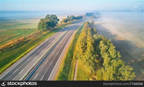Sunny Magical autumn foggy morning. Aerial view of highway with cars. Asphalt road covered in fog. Early misty dawn. M1 magistaral in Belarus