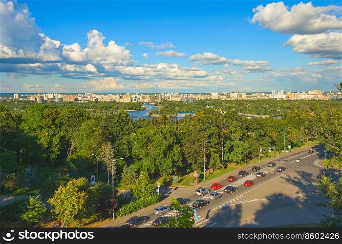 Sunny skyline of Kiev city on green banks of the Dnipro river with traffic on road, Ukraine