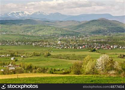 Sunny spring day in village and town on foothills. Mountains on background. Sunny green spring landscape.