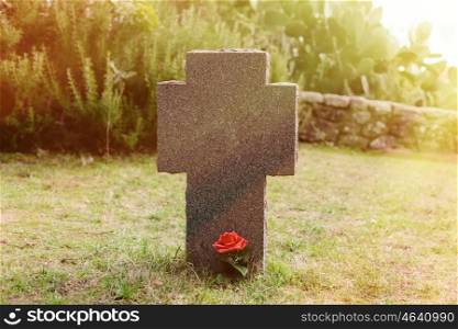 Sunny tomb with red flower next to the stone cross