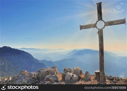 sunrise back of a cross at the top of the mountain under sky . cross at the top of mountain in the sun rising in blue sky 