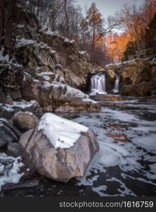 Sunrise glow hitting the trees behind the waterfall at Scott s Run Nature Preserve in Northern Virginia with a light dusting of snow.