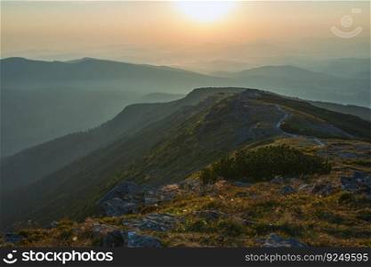 Sunrise in mountains. Natural mountain landscape with illuminated misty peaks, foggy slopes and valleys, blue sky with orange yellow sunlight. Amazing scene from Beskid Zywiecki in Poland