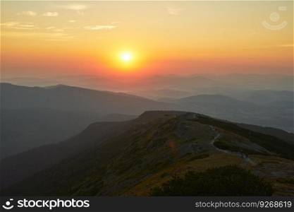 Sunrise in mountains. Natural mountain landscape with illuminated misty peaks, foggy slopes and valleys, blue sky with orange yellow sunlight. Amazing scene from Beskid Zywiecki in Poland