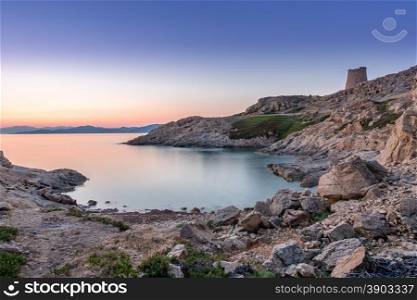 Sunrise in the bay at Ile Rousse in Corsica with a calm mediterranean sea and a Genoese tower in the foreground and mountains of the desert des agriates in the background