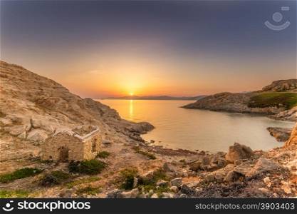 Sunrise in the bay at Ile Rousse in Corsica with an abandoned building in the foreground and Genoese tower and mountains of the desert des agriates in the background