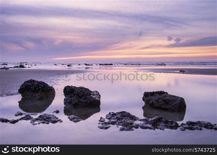 Sunrise landscape on rocky sandy beach with vibrant sky and clouds