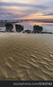 Sunrise landscape on rocky sandy beach with vibrant sky and clouds