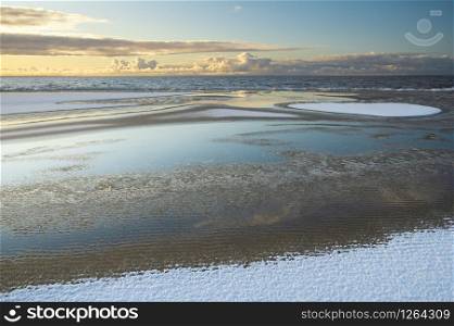 Sunrise light over the snowy beach of Baltic sea in winter morning, with the beautiful reflections of clouds in water