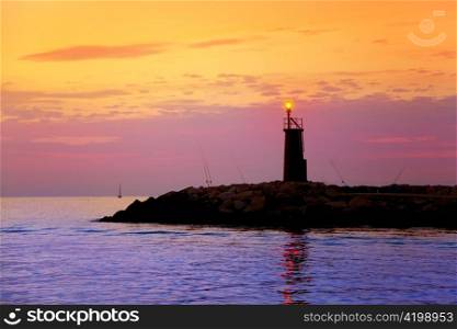 Sunrise lighthouse glowing in blue purple sea and orange sky