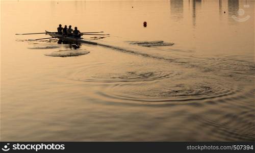 Sunrise lights up team of four rowers in canoe practicing in London Docklands. Team of four rowers practice in racing canoe