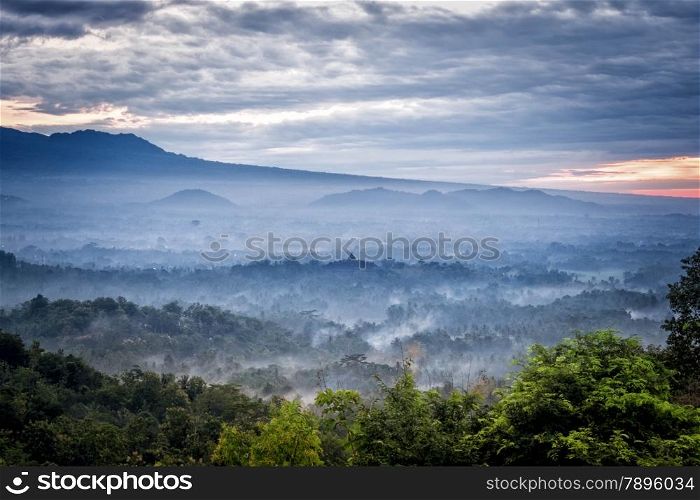 Sunrise over a valley with Borobudur temple in the distance