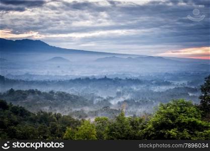 Sunrise over a valley with Borobudur temple in the distance