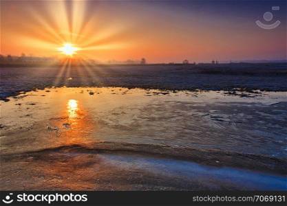 Sunrise over frozen fields and the reflection of the sun in the ice covering the field.Polska at the end of February.Horizontal view.