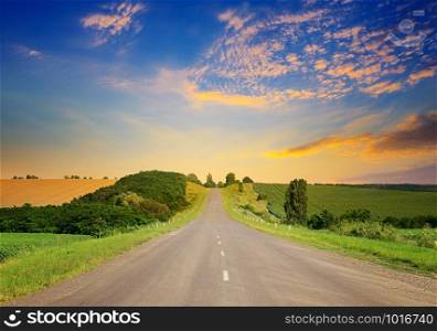 Sunrise over picturesque landscape. Straight road and fields illuminated rays sun.